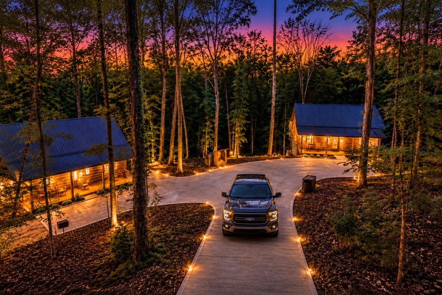 Two cabins lit at dusk among tall trees